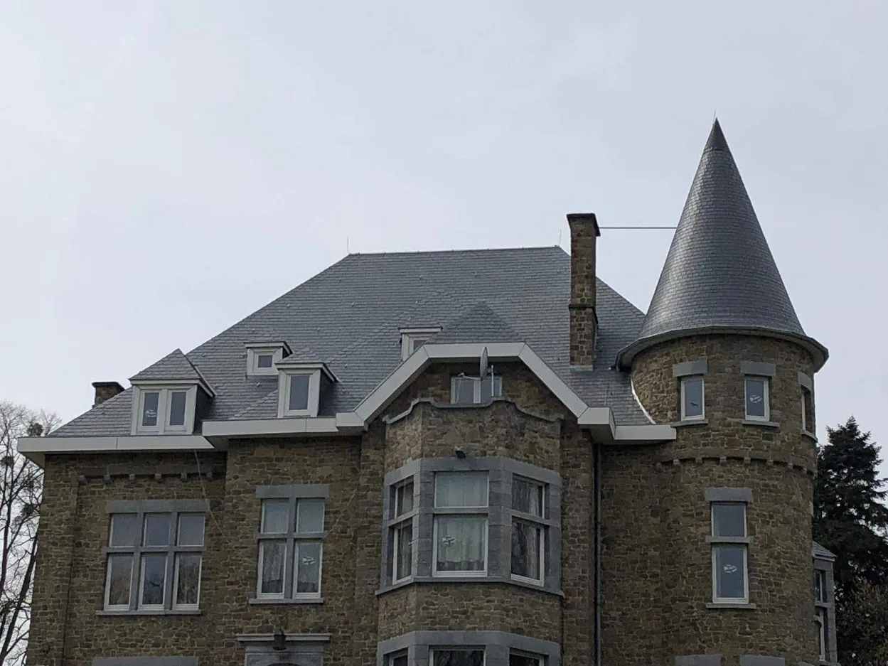 Toiture en ardoises rénovée sur une villa en pierre avec tourelle